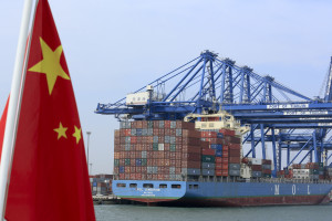A Chinese flag flies on a vessel moving past shipping containers being unloaded at a Tianjin Port Group Co. dock in Tianjin, China, on Wednesday, Sept. 12, 2012. The Chinese government is trying to meet a 7.5 percent economic growth target set in March, which would already be the weakest expansion since 1990. Photographer: Nelson Ching/Bloomberg